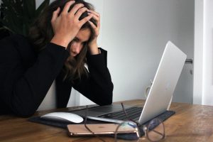 mental health and recruitment shown through a lady holding her head in her hands looking at her work computer in a state of upset
